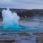 strokkur-geyser-surrounded-by-hills-under-a-cloudy-sky-in-the-evening-in-iceland-scaled-e1655366993723.jpg